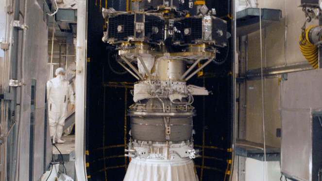 A scientist in a clean suit inspects a large satellite mounted in a ValveTech Inc. testing facility.